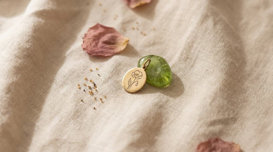 Goldener Anhänger mit gravierter Mohnblume neben einem grünen Peridot auf hellem Leinen