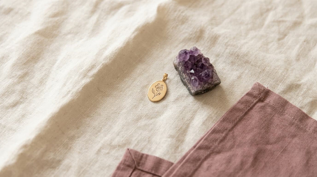 Goldener Anhänger mit graviertem Veilchen neben einem violetten Amethyst auf hellem Leinen