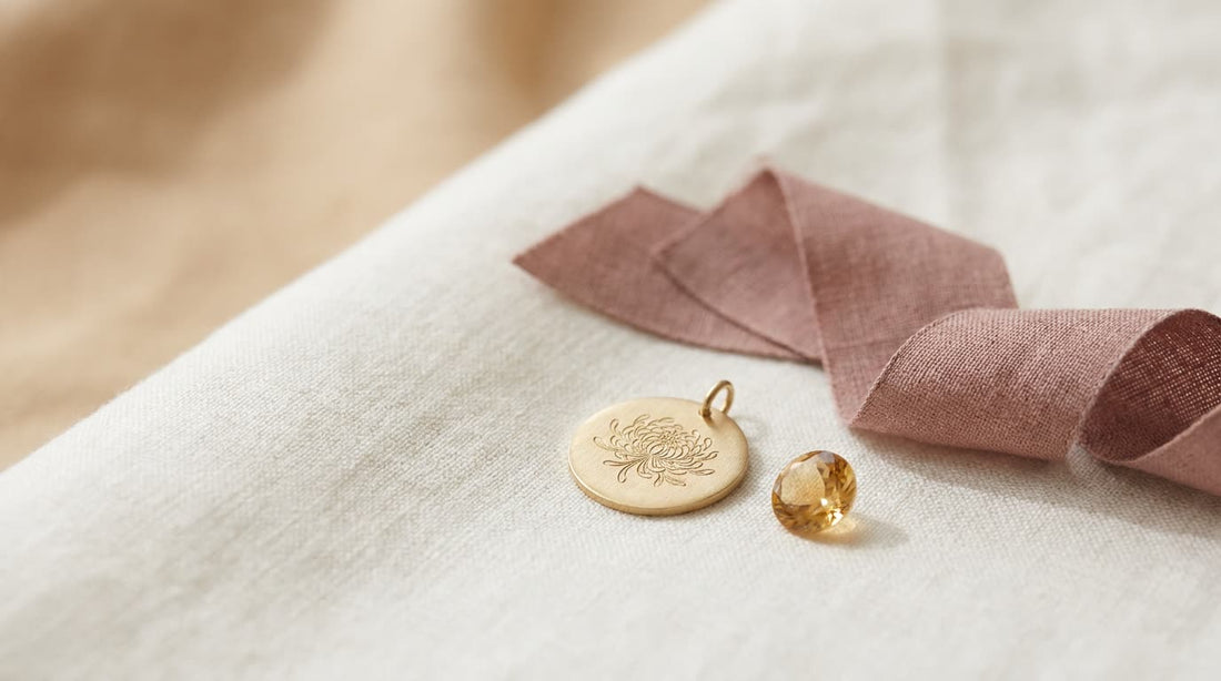 Goldener Anhänger mit gravierter Chrysantheme neben einem goldgelben Topas auf hellem Leinen