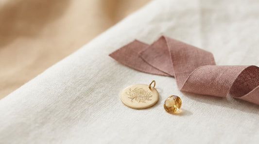 Goldener Anhänger mit gravierter Chrysantheme neben einem goldgelben Topas auf hellem Leinen