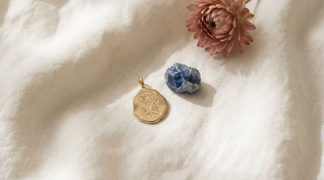 Goldener Anhänger mit gravierter Prunkwinde neben einem blauen Saphir auf hellem Leinen